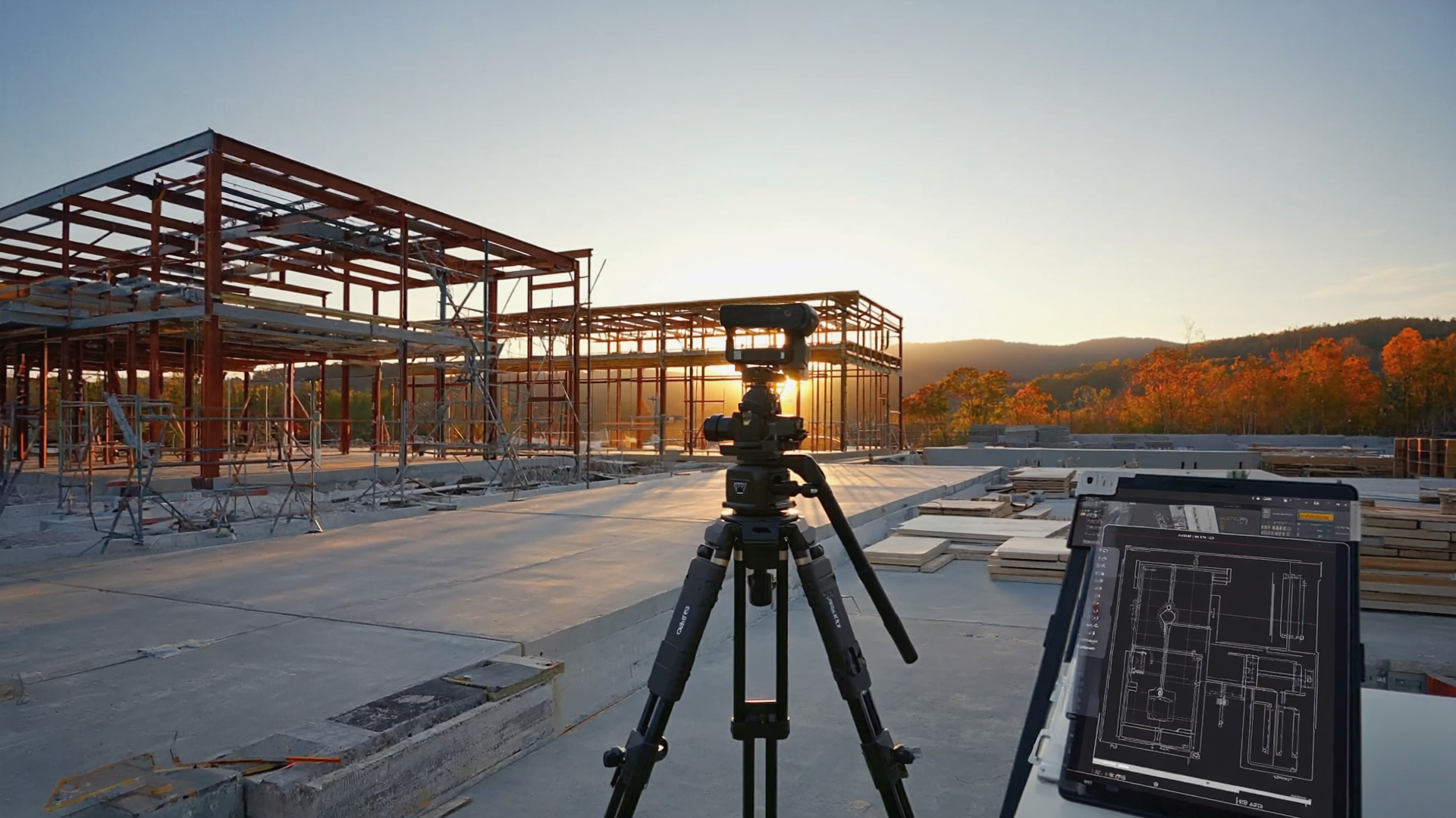 Construction site surveying with tripod camera and digital blueprint on tablet at sunset, steel frame commercial building under development